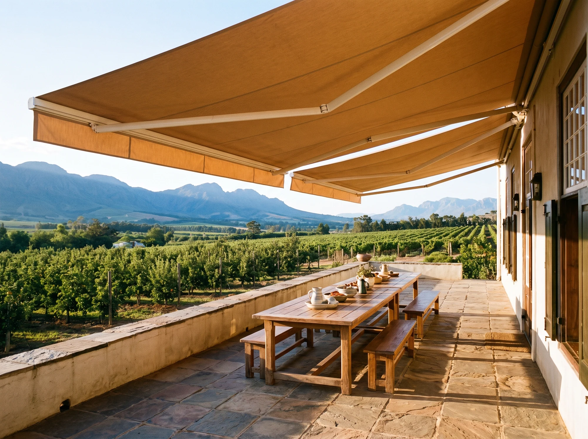 Folding-arm awning extended over a long stoep table on a Simondium wine farm, vineyard and mountain view